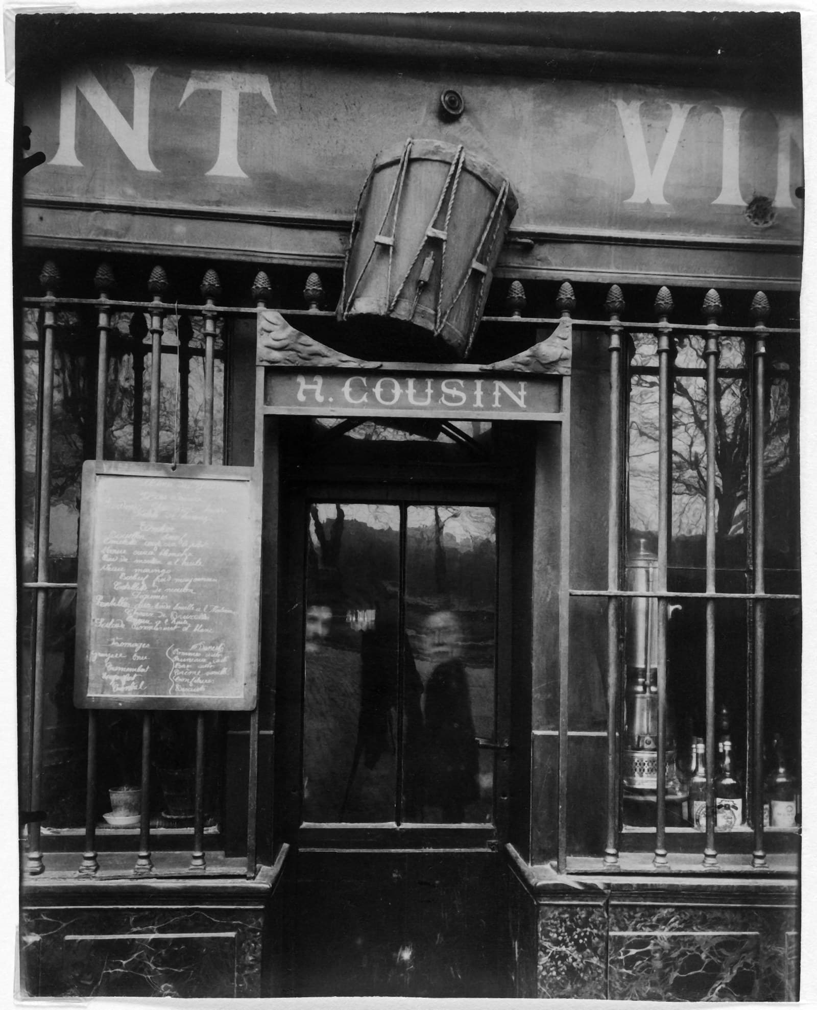 La façade d’un restaurant parisien : un tambour suspendu en guise d’enseigne, le nom du patron peint au-dessus de la porte, un menu affiché à côté.