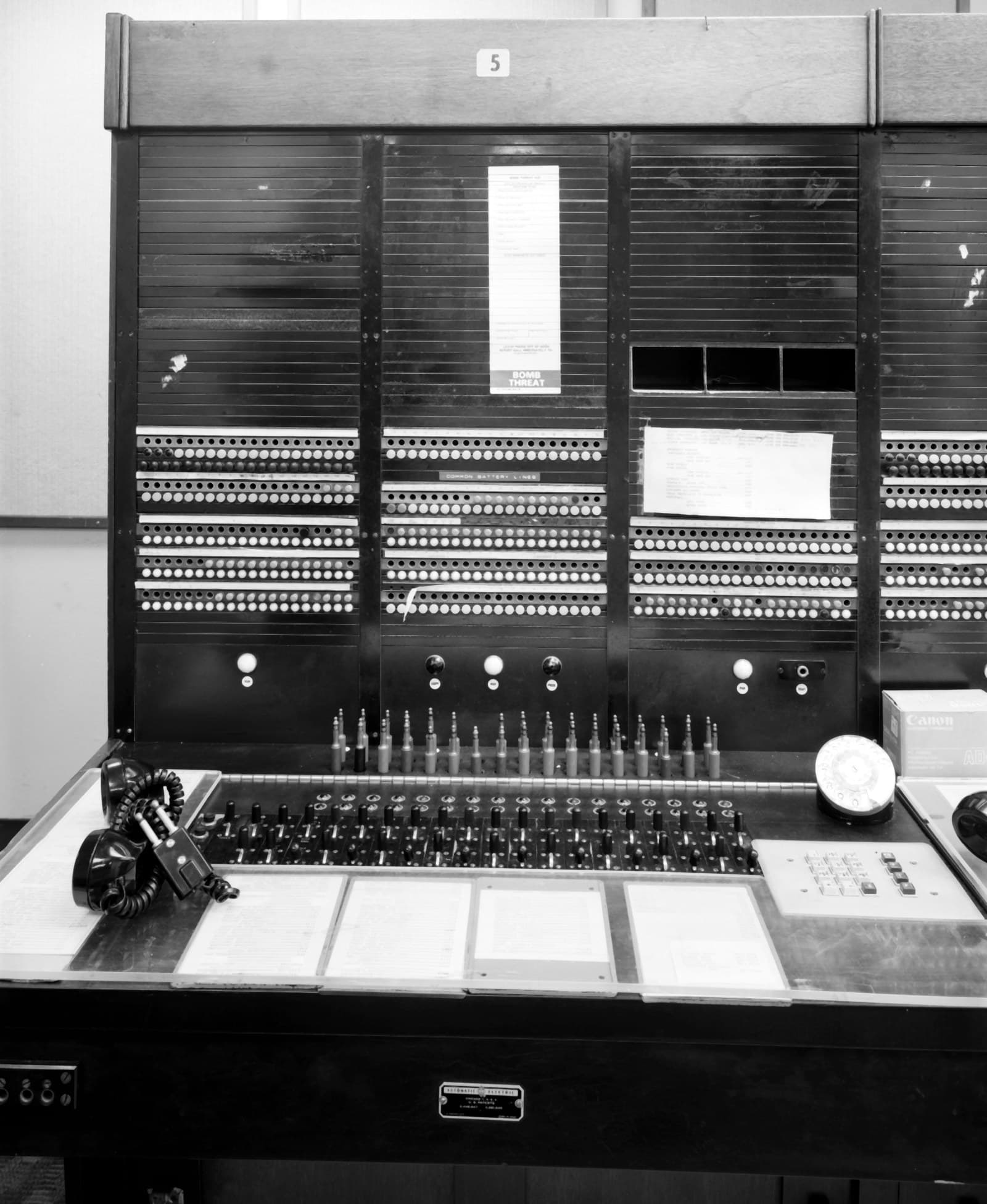 Un ancien panneau de brassage téléphonique : des rangées de prises et de voyants, un pupitre de commande et ses fiches.