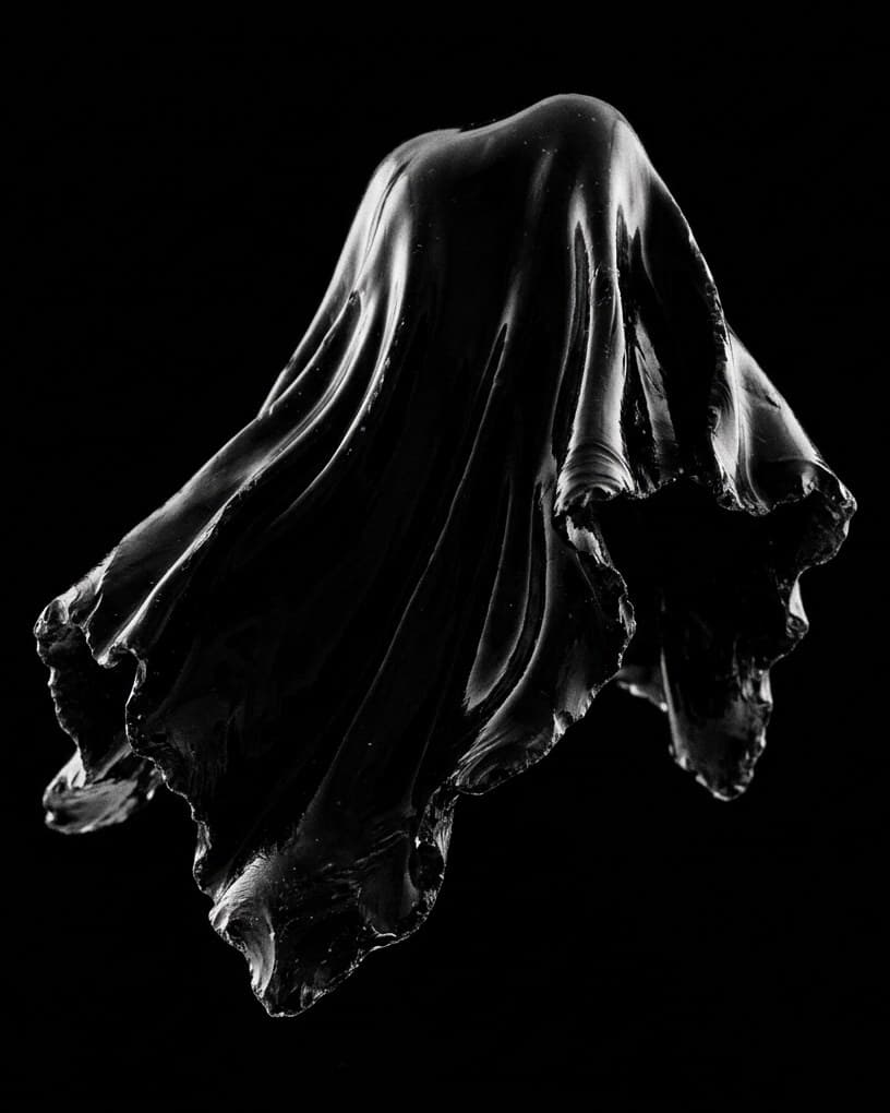 Un drapé de verre noir, comme un tissu figé en plein mouvement, sur un fond noir.
