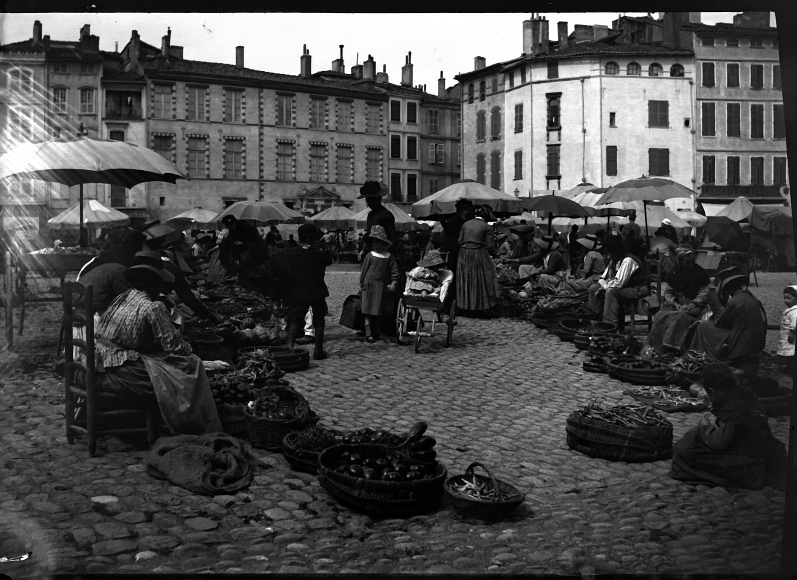 Le marché de la place des Salins à Toulouse : des marchandes assises derrière leurs paniers sous de grands parapluies, des clients entre les étals.